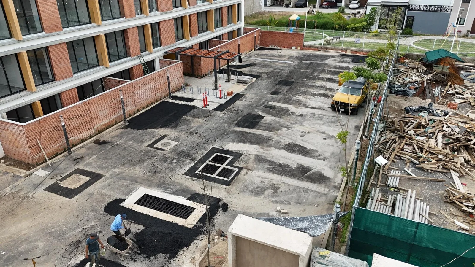 Estacionamiento de la Torre 1 recibiendo la carpeta asfáltica, con la pérgola de celosía al fondo